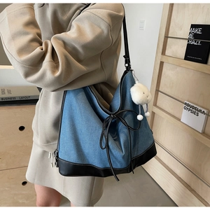 Detail of blue denim tote bag featuring white contrast stitching and a bow accent
