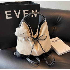 Detail of beige woven tote bag featuring a large black leather bow and white cloud charm