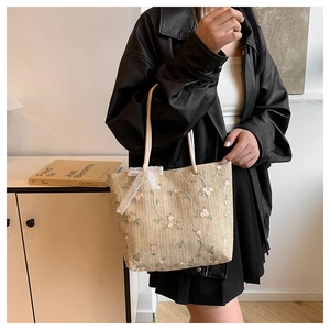 Dettaglio della borsa tote in paglia intrecciata con ricami floreali e fiocco in pizzo