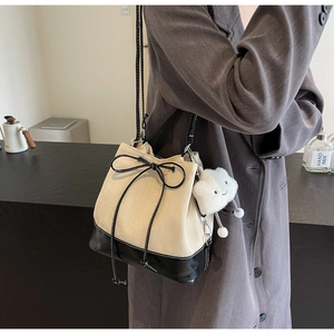 Detail of canvas and black leather bucket bag with a plush cloud charm and bow knot