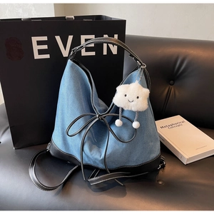 Detail view of denim tote bag with leather trim, stitching and white plush cloud charm
