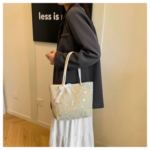 Dettaglio del ricamo floreale e fiocco in tulle sulla borsa tote in paglia intrecciata