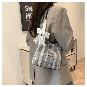 Close-up of gray plaid canvas bucket bag with white lace ribbon bow on a model