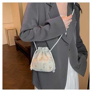 Dettaglio della borsa a secchiello in paglia beige con ricamo floreale e coulisse