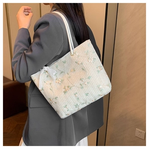Dettaglio della borsa tote in paglia con ricami floreali e accenti di fiocco bianco