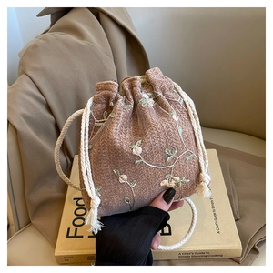 Dettaglio della borsa a secchiello intrecciata color avena con ricami floreali e lacci