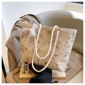 Dettaglio di ricamo floreale e fiocco di pizzo su una borsa tote in paglia intrecciata beige