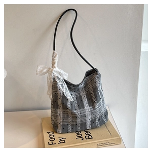 Close-up of grey plaid bucket bag with a delicate white lace bow and black strap