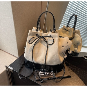 Detail of drawstring bucket bag with beige herringbone fabric and black leather base