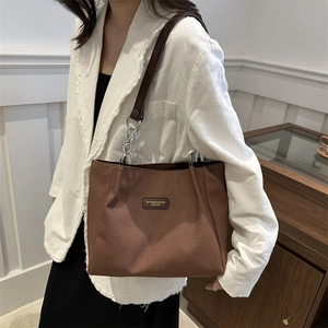 Brown minimalist tote bag with leather straps and metal chain on model in white blazer