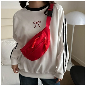 Detail of red canvas crossbody chest bag with woven zipper pulls and adjustable strap