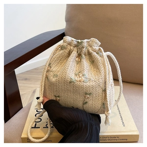 Dettaglio della borsa a secchiello in paglia con elegante ricamo floreale e chiusura a corda