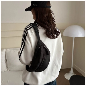 Detail view of black nylon crossbody bag featuring adjustable strap and sleek curved zipper