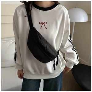 Detail of a casual black nylon crossbody bag worn over a white sweatshirt with embroidery