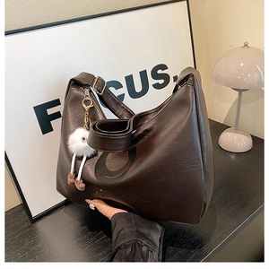 Detail der hobo-tasche in dunkelkaffee glänzendem leder mit süßem plüschpuppen-anhänger