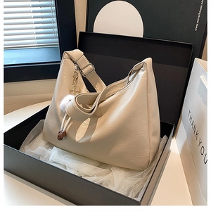 Detail of a creamy white matte leather tote bag with a plush charm in a gift box