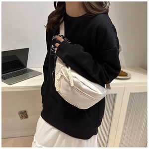 Detail of a minimalist white crossbody chest bag with adjustable strap worn by a model