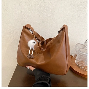 Detail der braunen Hobo-Tasche aus strukturiertem Kunstleder mit weißem Plüsch-Anhänger