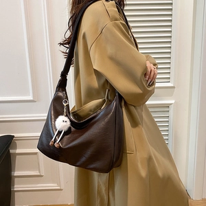 Minimalistische dunkelbraune Halbmond-Tasche mit Plüsch-Anhänger am Trenchcoat-Model