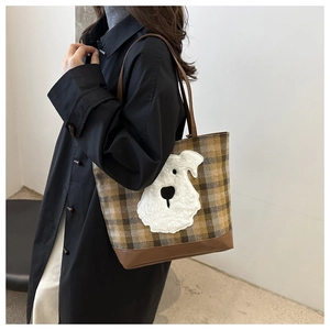 Detail of checkered tote bag with plush dog patch and leather straps on model