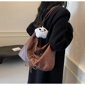 Close-up of brown vintage hobo tote bag featuring side lace-up details and a panda plush charm