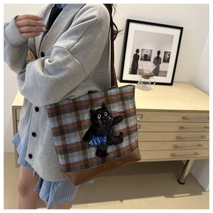 Detail of checkered tote bag with cat embroidery and fish accent on model's shoulder