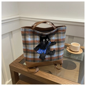 Detail of plaid tote bag with cute black cat plush patch and brown leather handles