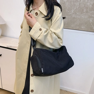 Minimalist black nylon cylinder crossbody bag with fashion tag on a female model