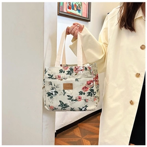 Bolsa de almuerzo de lona con flores rojas y etiqueta de cuero sostenida por modelo