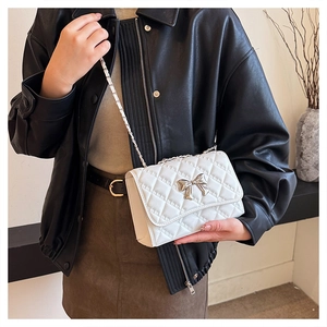 Chic white quilted shoulder bag with chain strap and bow detail on a black jacket