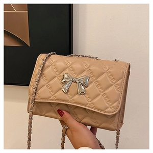 Close-up of beige quilted shoulder bag with silver bow clasp and woven chain strap