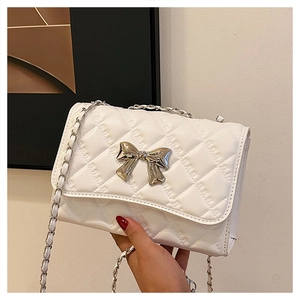 Detail of white quilted handbag featuring silver metal bow clasp and chain strap