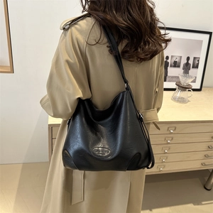 Minimalist black pebbled leather tote bag with embossed logo worn by a model in a trench coat