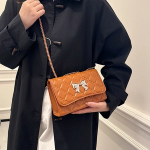Caramel quilted crossbody bag with silver bow clasp and chain strap on model