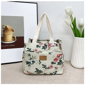 Detalle de la bolsa de almuerzo de lona floral con bolsillo exterior y logo de cuero