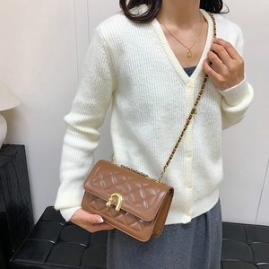 Brown quilted chain shoulder bag with gold horseshoe buckle on model in minimalist setting