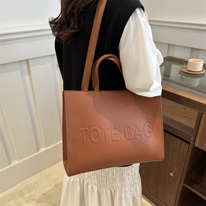 Minimalist large brown leather tote bag with embossed logo worn by a model in a cozy room