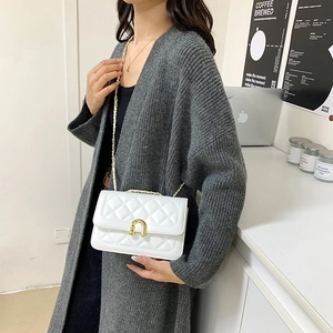 White quilted chain crossbody bag with golden horseshoe clasp worn by a fashion model