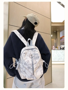 Detail of cream backpack with bear prints and woven zipper pulls on a model