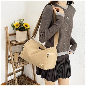Dettaglio borsa a tracolla beige cilindrica con ampia cinghia e logo dorato