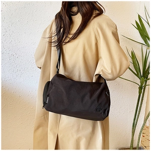 Grande borsa a tracolla in nylon nero su una modella in trench beige per un look trendy