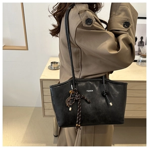 Dettaglio della borsa tote in pelle nera con scritta FASHION su modella in trench