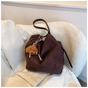 Detail of a dark brown suede tote bag with a cute teddy bear charm on an ivory chair