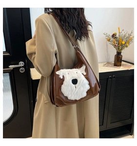 Brown leather shoulder bag featuring a white plush dog detail shown on model in home setting