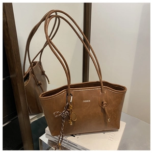 Dettaglio di borsa tote in ecopelle marrone con ciondoli dorati e logo fashion inciso