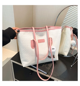 White embossed tote bag with pink straps and plush charm on a wooden surface