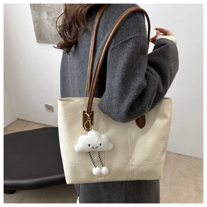 Detail of a large cream tote bag with dark brown straps and a cute cloud charm accessory
