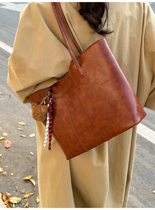 Detail of vintage brown leather tote bag with plush bear charm and striped silk scarf