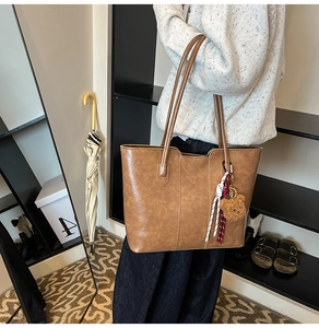 Detail of a brown tote bag with leather texture and a cute plush bear charm accessory