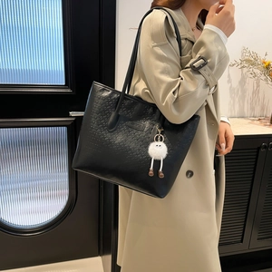 Fashionable black embossed leather tote bag with plush charm and stylish long shoulder straps